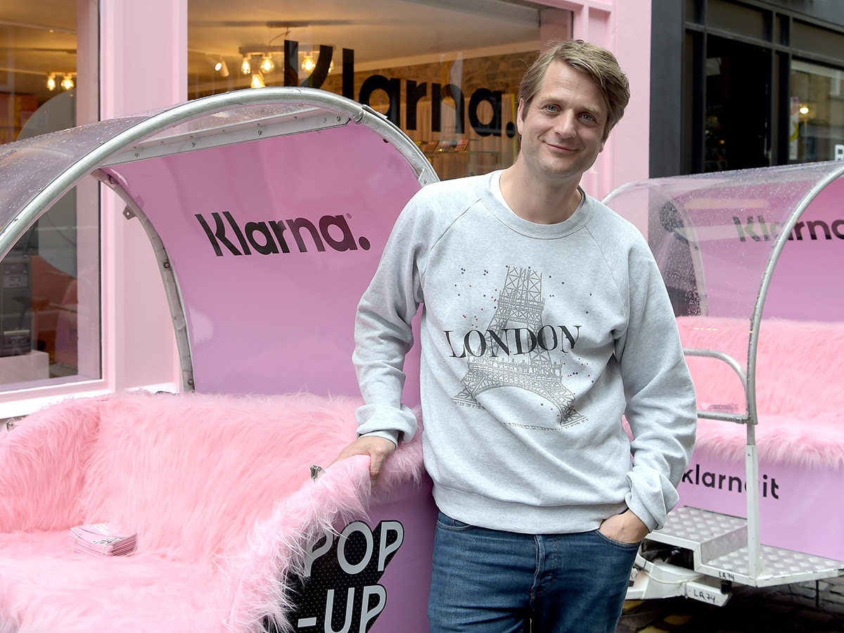 Klarna co-founder and CEO Sebastian Siemiatkowski poses in front of a Klarna-branded storefront and vehicle.
